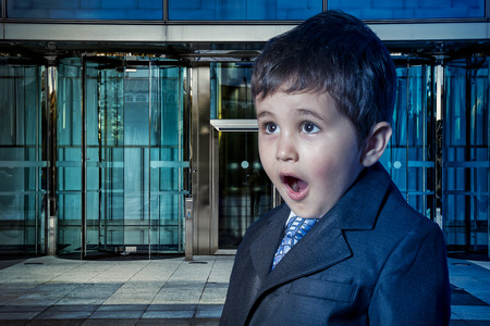 Education, child dressed businessman with hands in his tie and skyscrapers in the backgroundの写真素材