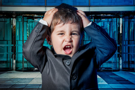 Serious child dressed businessman with hands in his tie and skyscrapers in the backgroundの写真素材