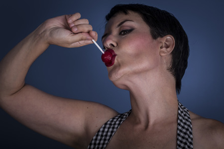 happy young woman with lollypop  in her mouth on blue backgroundの写真素材