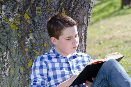 Young boy reading a book in the woods with shallow depth of field and copy spaceの写真素材