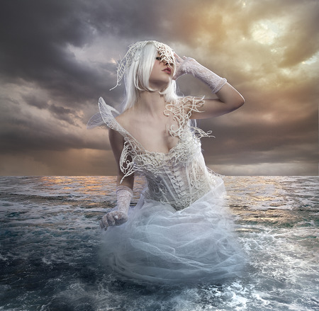 the forces of nature, blonde woman on the rocks with the sea raging and powerfulの写真素材