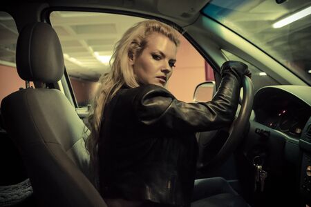 blonde in car driving at night, dressed in jeans and leather jacketの写真素材
