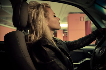 Vintage, blonde in car driving at night, dressed in jeans and leather jacketの写真素材