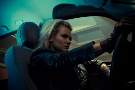 blonde in car driving at night, dressed in jeans and leather jacketの写真素材