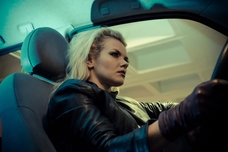 blonde in car driving at night, dressed in jeans and leather jacketの写真素材