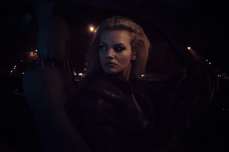 Traffic, aggressive look blonde driving a car at night in the cityの写真素材