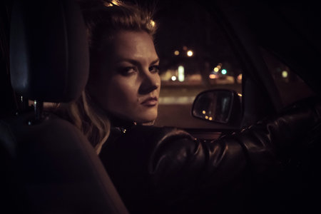 Lifestyle, aggressive look blonde driving a car at night in the cityの写真素材