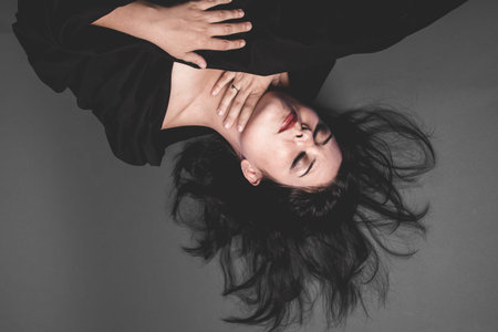 Death, gothic dark woman with large black cloth on gray background, Sadness