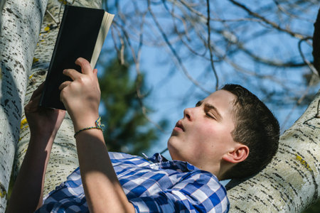 Spring Young boy reading a book in the woods with shallow depth of field and copy space