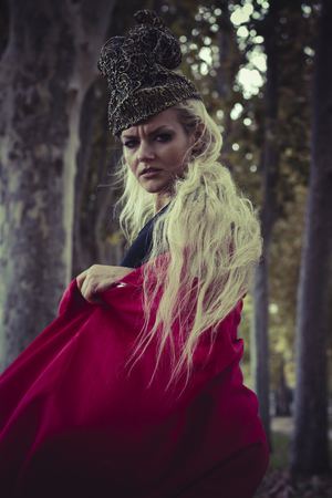 beautiful blond woman with red cape to the wind in a forest, romance and fantasy imageの写真素材