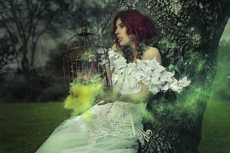 haired girl with white dress of leaves in a forest with colored smokeの写真素材