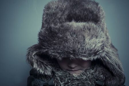 Funny child with fur hat and winter coat, cold concept and stormの写真素材