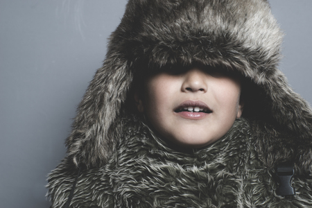 Funny child with fur hat and winter coat, cold concept and stormの写真素材