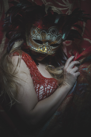 Party, Blonde with gold mask on red cloth embroidered golden thread, mystery and sensualityの写真素材