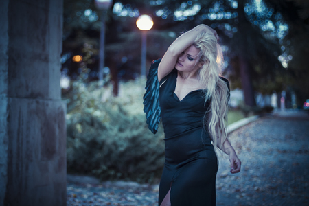 an angel in the city, beautiful blonde with long hair dressed in black and with black wingsの写真素材