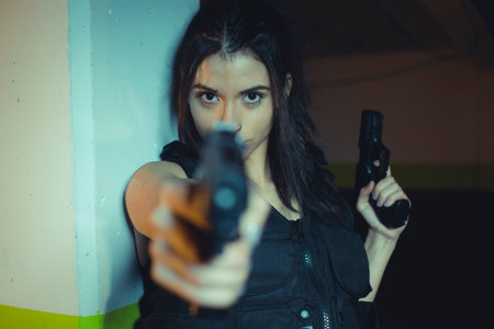 Army brunette girl with gun in a garage in attitude shoot, dressed in bulletproof vest