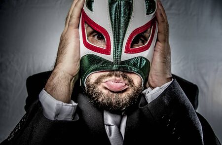 Angry businessman with mask of Mexican fighter, dressed in suit and tieの写真素材