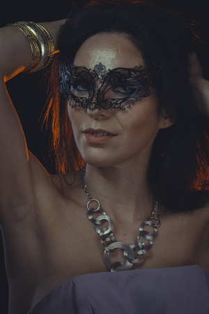 Seductive, Femininity and eroticism, brunette woman with mask of black fruity and gold and silver jeweleryの写真素材