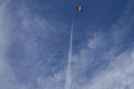 Kite of rainbow colors on a blue sky with light white cloudsの写真素材