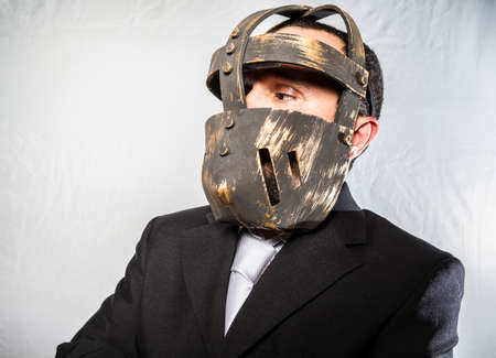 Angry businessman with iron mask on his face, is dressed in suit and tieの写真素材