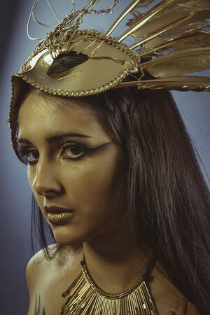 Beautiful brunette with golden crown, made with feathers and golden chains. Goddess of fantasyの写真素材