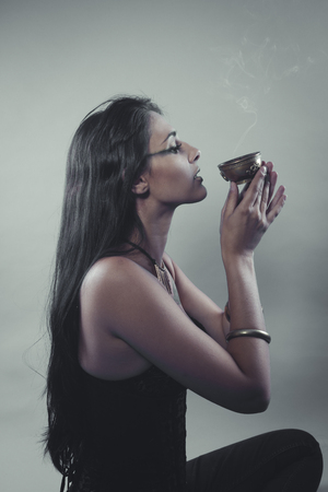 Witchcraft, Tribute and prayer. Beautiful brunette with bronze bowl and incense in a gesture of faithの写真素材