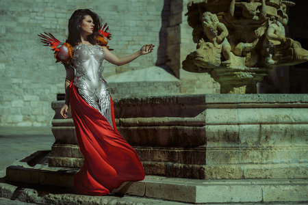 Glamour Queen in silver and gold armor, beautiful brunette woman with long red coat and brown hairの写真素材