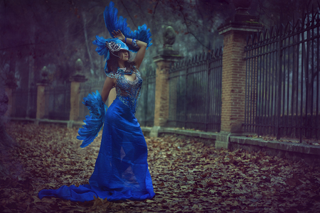 Beautiful brunette girl in a suit made of blue wires, bears bird wings and colorful feathers helmetの写真素材