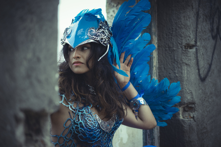Gothic beautiful brunette girl in a suit made of blue wires, bears bird wings and colorful feathers helmetの写真素材
