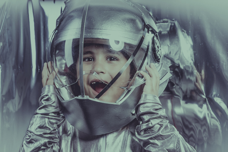 Future, Boy playing to be an astronaut with space helmet and metal suit over silver backgroundの写真素材