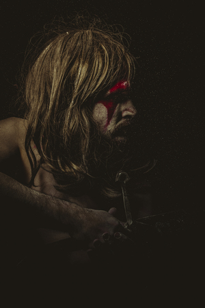 Strong, Wild warrior with metal sword and war paintings on the face, long hairの写真素材