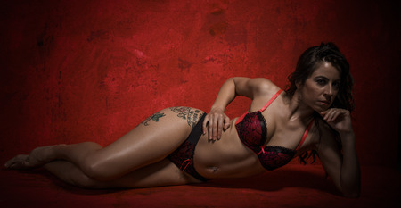 Erotic, Beautiful brunette woman with sensual lingerie on textured background in red. sexy and provocative posesの写真素材