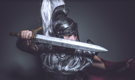 Violence Roman gladiator, wrestler and warrior of Rome with helmet and red cloak, carries an iron sword, beard and long hair.の写真素材