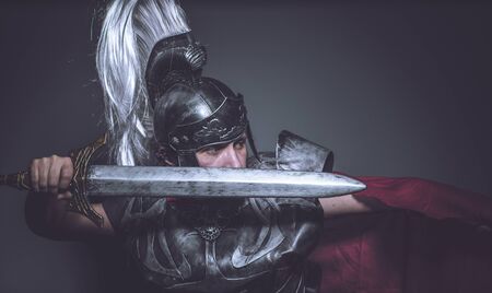 Roman gladiator, wrestler and warrior of Rome with helmet and red cloak, carries an iron sword, beard and long hair.の写真素材