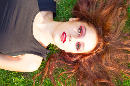 beautiful redhead hispanic girl lying on the grass with serene and sensual lookの写真素材