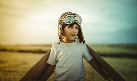 Happy child playing with toy wings against summer sky background. Retro vintage toned. Travel and adventure conceptの写真素材