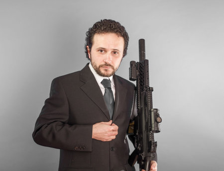 Serious confident businessman with machine gun in room. Looking in camera.