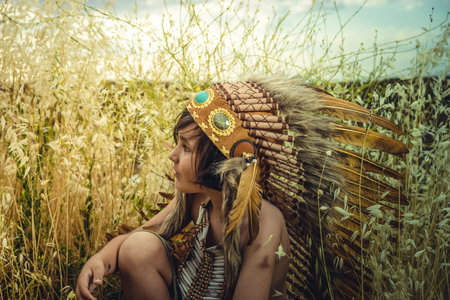 Child dressed as an American Indian at sunset, wearing an Indian feather plume and breastplate of...