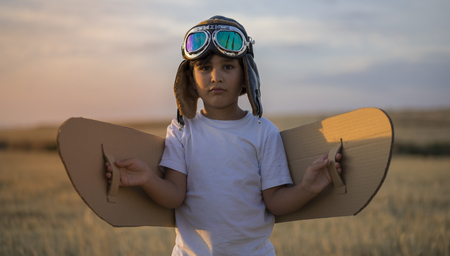 Summer sunset, Boy playing to be airplane pilot, funny guy with aviator cap and glasses, carries in his hand a plane made of paperの写真素材