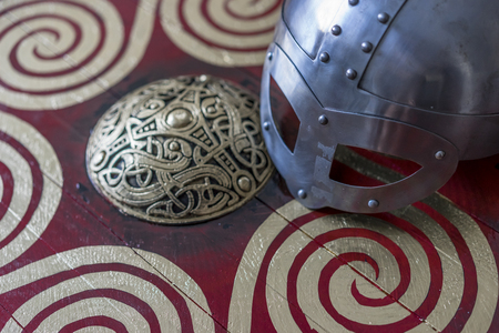 Danger, viking helmet with chain mail on a red shield with golden shapes of sun, weapons for warの写真素材
