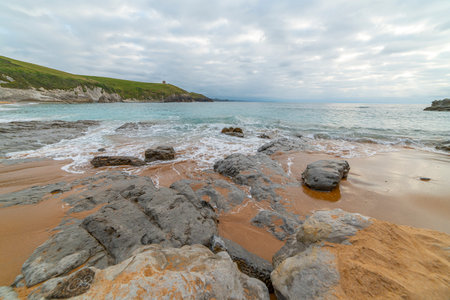 Tranquil scene of Tagle Beach in Cantabria, Spain, showcasing rugged rocks, gentle waves, and an expansive horizon. Perfect for travel, nature, and coastal themes.の写真素材