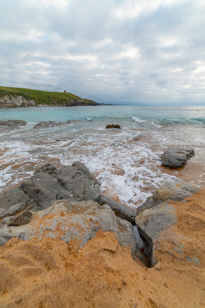Tranquil scene of Tagle Beach in Cantabria, Spain, showcasing rugged rocks, gentle waves, and an expansive horizon. Perfect for travel, nature, and coastal themes.の写真素材