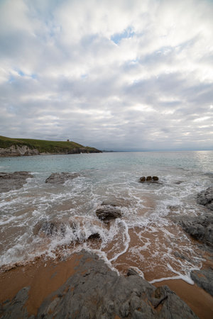 Tranquil scene of Tagle Beach in Cantabria, Spain, showcasing rugged rocks, gentle waves, and an expansive horizon. Perfect for travel, nature, and coastal themes.の写真素材