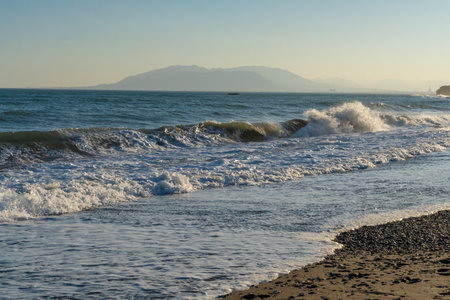 Powerful waves break along the shores of Malaga, Spain, with distant mountains visible on the horizon. Ideal for themes of coastal energy, nature, and scenic seascapesの写真素材