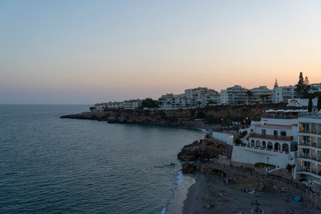 A tranquil dusk view of Nerja's coastline, featuring cliffside buildings and the calm Mediterranean Sea. Perfect for travel, sunset, and coastal themes highlighting Spain's beauty.の写真素材
