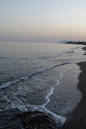 Gentle waves lap the shore at dusk on a tranquil beach in MÃ¡laga, Spain. Perfect for themes of relaxation, coastal serenity, and nature's beauty.の写真素材