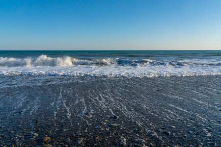 Powerful waves break along the shores of Malaga, Spain, with distant mountains visible on the horizon. Ideal for themes of coastal energy, nature, and scenic seascapesの写真素材