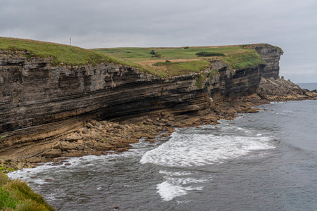 Majestic coastal cliffs with layered rock formations and lush greenery overlooking the sea in Cantabria, Spain. Perfect for landscape, travel, and nature themes.の写真素材