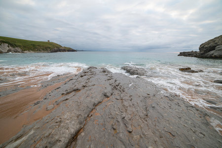 Tranquil scene of Tagle Beach in Cantabria, Spain, showcasing rugged rocks, gentle waves, and an expansive horizon. Perfect for travel, nature, and coastal themes.の写真素材