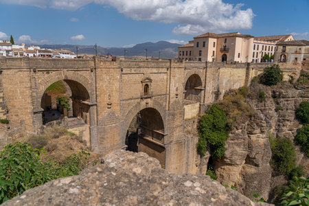 The iconic Puente Nuevo Bridge in Ronda, Spain, gracefully arches over the deep Tajo Gorge, with historic buildings perched on the cliffs. Perfect for themes of architecture, history, and travel.の写真素材